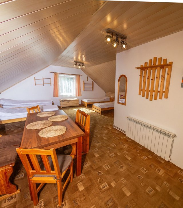 Apartament na poddaszu ze skosami: cztery pojedyncze łóżka, dwa złączone razem, i drewniany stół z krzesłami