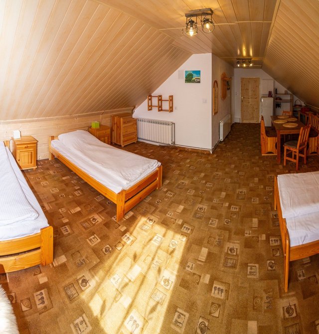 Apartament na poddaszu z drugiej strony: pojedyncze łóżka pod skosem, w głębi stół i aneks kuchenny